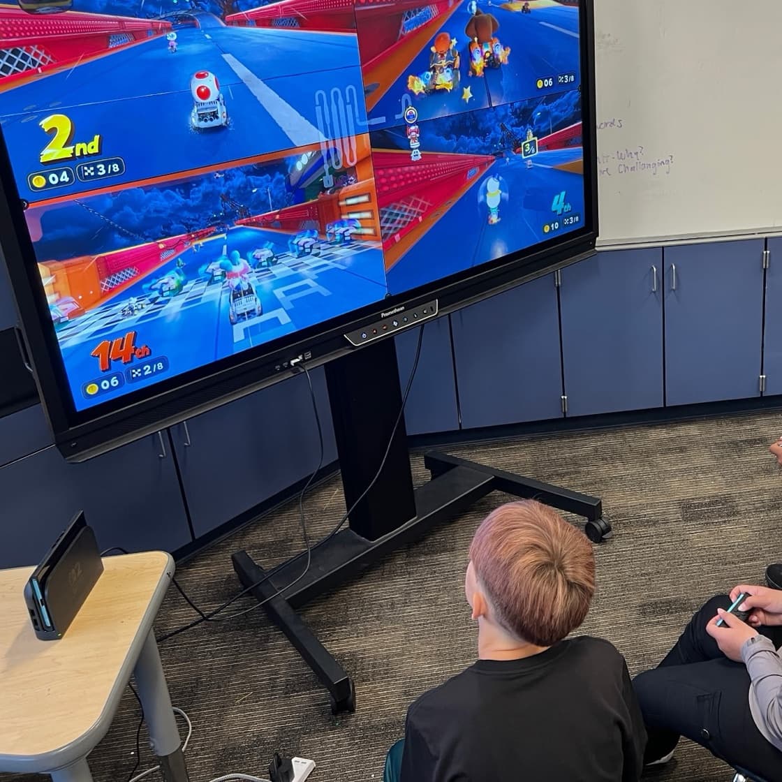 Students playing a multiplayer racing game on a classroom display during an iAttend esports session.